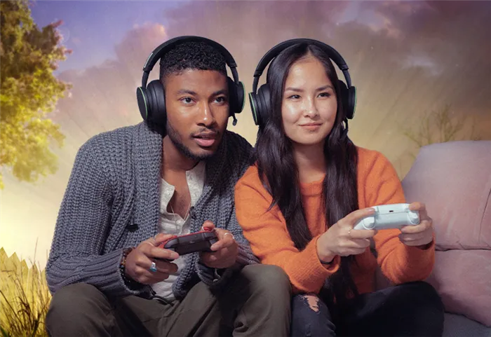 Два человека с гарнитурами сидят на диване и вместе играют на Xbox