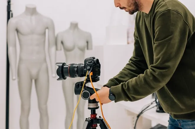 Мужчина устанавливает камеру Canon EOS на штатив в фотостудии, подключив к ней внешний источник питания и кабель подключения USB.